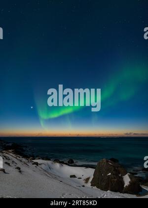 Spektakuläre, tanzende grüne, kräftige Nordlichter über dem berühmten runden Felsstrand in der Nähe von Uttakleiv auf den Lofoten-Inseln in Norwegen im klaren Winter Stockfoto