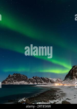 Spektakuläre, tanzende grüne, kräftige Nordlichter über dem berühmten runden Felsstrand in der Nähe von Uttakleiv auf den Lofoten-Inseln in Norwegen im klaren Winter Stockfoto