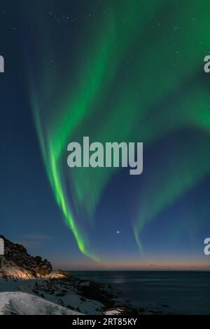 Spektakuläre, tanzende grüne, kräftige Nordlichter über dem berühmten runden Felsstrand in der Nähe von Uttakleiv auf den Lofoten-Inseln in Norwegen im klaren Winter Stockfoto