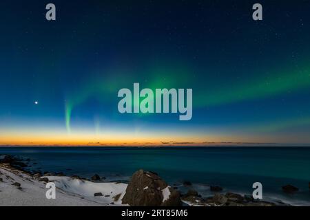 Spektakuläre, tanzende grüne, kräftige Nordlichter über dem berühmten runden Felsstrand in der Nähe von Uttakleiv auf den Lofoten-Inseln in Norwegen im klaren Winter Stockfoto