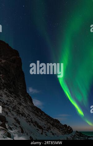 Spektakuläre, tanzende grüne, kräftige Nordlichter über dem berühmten runden Felsstrand in der Nähe von Uttakleiv auf den Lofoten-Inseln in Norwegen im klaren Winter Stockfoto