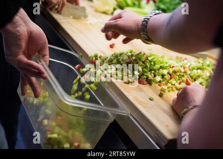 Menschliche Hände schaufeln Würfel von geschnittenem Rhabarber aus Holzschnitt Board in Kunststoffschale für die weitere Verarbeitung in der Küche Stockfoto