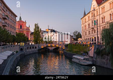 Die Promenade am Fluss Ljubljanica in der slowenischen Hauptstadt Stadt Ljubljana mit der Dreifachbrücke und berühmten rosa franziskaner kirche am Abend Stockfoto