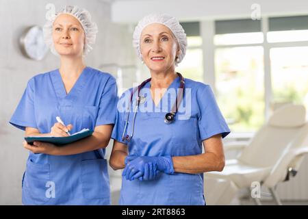 Porträt zweier positiver Ärztinnen in blauer Uniform vor dem Hintergrund des Klinikinnenraums Stockfoto