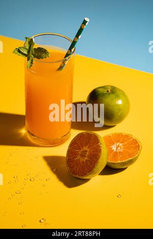 Saft aus frisch gepressten kalten Orangen mit Eis auf blaugelbem Hintergrund. Pop-Art-Stil. Stockfoto