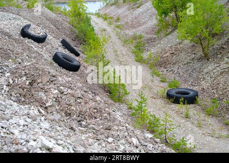 Vier alte Reifen, die illegal auf Schmutz geworfen wurden, wurden weggeworfen. Dolomitbrüche mit Abfall. Umweltfreundlich. Aidu-Steinbruch, Estland. Stockfoto