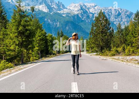 Ein Tourist im Sommer zu Fuß auf der Straße im Valbona Tal neben Bäumen, Theth Nationalpark, Albanischen Alpen, Valbona Albanien Stockfoto