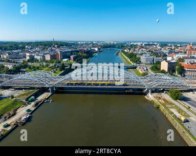 Neue dreifach gebundene Eisenbahnbrücke mit laufendem Zug über die Weichsel in Krakau, Polen, weitere Brücken, Altstadt und touristischer Beobachtungsballon Stockfoto