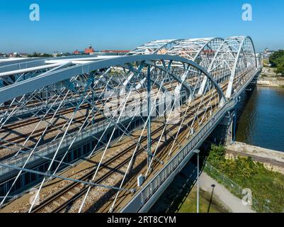 Dreifach gebundene Eisenbahnbrücke mit vier Gleisen über die Weichsel in Krakau, Polen. Altstadt im Hintergrund. Drohnenansicht aus der Luft. Stockfoto