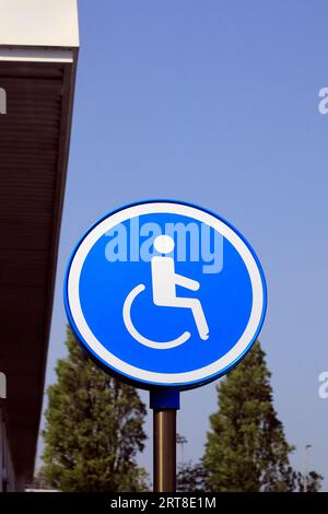 Behindertenparkplatz auf der runden Seite - Mann im Rollstuhl vor blauem Hintergrund, der Parkplätze in der Nähe von Eingängen anzeigt, um Zugang zu erhalten Stockfoto