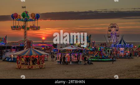 Hell beleuchteter Jahrmarkt mit Fahrten am Strand vor einem wunderschönen roten Sonnenuntergang am St annes on SEA internationales Kite Festival 2023 Stockfoto