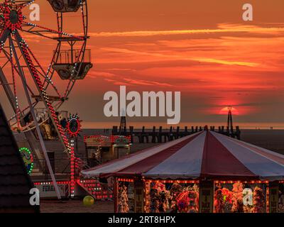 Hell beleuchteter Jahrmarkt mit Fahrten am Strand vor einem wunderschönen roten Sonnenuntergang am St annes on SEA internationales Kite Festival 2023 Stockfoto