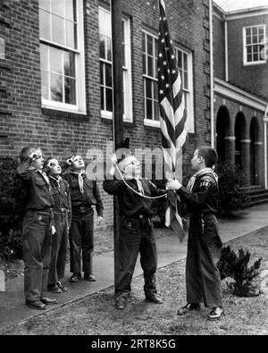 Junge Mitglieder eines Cub Scout-Geländes nehmen in den 1950er Jahren an einer US-amerikanischen Flaggenhisserungszeremonie Teil Stockfoto