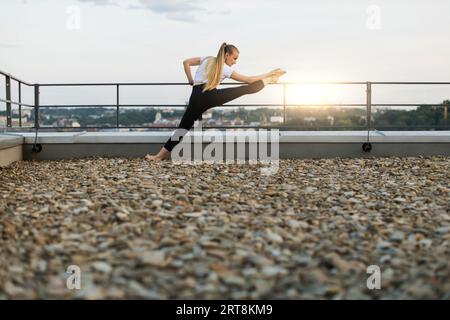 Sportlerin, die die Beine vorne spreizt, teilt sich auf dem Dachhandlauf auf Stockfoto