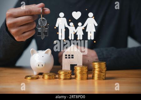 Der Mann hält Schlüssel und Münzen, die ein Haus bilden sollen, mit gestapelten Münzen, die die steigenden Zinssätze veranschaulichen Stockfoto
