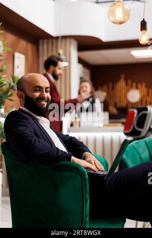 Gäste bereiten sich auf Geschäftstreffen vor und arbeiten vor der Zimmerregistrierung am Laptop in der Lobby im Loungebereich. Geschäftsmann, der produktive Arbeit leistet, um Zeit zu verlieren, während er auf eine Konferenz wartet. Stockfoto