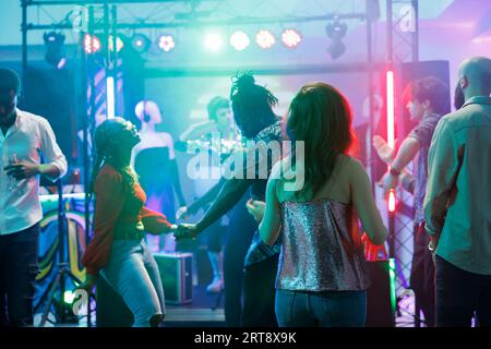Partytänzer machen Bewegungen auf der Tanzfläche, während sie Spaß haben und sich im Nachtclub entspannen. Die Gäste besuchen die Diskothek und tanzen, während sie die Musik im Club genießen, der von Bühnenlichtern beleuchtet wird Stockfoto