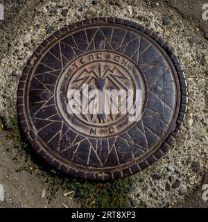 Ein sowjetischer gusseiserner Schachtdeckel mit der kyrillischen Inschrift „ТЕЛЕФОН“ (Telefon) und den Initialen „МС“ auf einer Straße im Bezirk Chugureti in Tiflis, Georgien. Die Mannlochabdeckung ist Teil der sowjetischen Telekommunikationsinfrastruktur der Stadt und ist trotz der Auflösung der UdSSR im Jahr 1991 bis heute in Gebrauch. Der Deckel befindet sich in Chugureti, Tiflis, Georgien Stockfoto