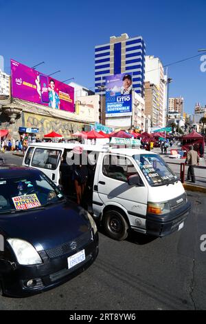 La Paz, BOLIVIEN; 11. September 2023: Ein Minibus-Assistent ruft die Passagiere vor einer Horde mit dem bolivianischen Präsidenten Luis Arce Catacora auf, um die "Industrialisierung von Lithium, einen großen Schritt in Richtung einer nachhaltigen Zukunft Boliviens" in La Paz zu fördern. Bolivien verfügt über einige der größten Lithiumreserven der Welt in der Salar de Uyuni-Saline, deren Entwicklung für die Wirtschaftspolitik der Regierung von zentraler Bedeutung ist. In diesem Jahr hat Bolivien Vereinbarungen mit dem chinesischen Batteriehersteller CATL und der Citic Guoan Group sowie dem russischen Staatsunternehmen Rosatom als Partner zur Entwicklung dieser Ressourcen unterzeichnet. Stockfoto