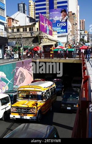 La Paz, BOLIVIEN; 11. September 2023: Ein alter öffentlicher Kleinbus im Av Villazon-Tunnel, mit dem bolivianischen Präsidenten Luis Arce Catacora auf einer Horde, die die "Industrialisierung von Lithium, einen großen Schritt in Richtung einer nachhaltigen Zukunft für Bolivien" im Hintergrund fördert. Bolivien verfügt über einige der größten Lithiumreserven der Welt in der Salar de Uyuni-Saline, deren Entwicklung für die Wirtschaftspolitik der Regierung von zentraler Bedeutung ist. In diesem Jahr hat Bolivien mit dem chinesischen Batteriehersteller CATL und der Citic Guoan Group und dem russischen Staatsunternehmen Rosatom Vereinbarungen zur Entwicklung dieser Ressourcen unterzeichnet. Stockfoto