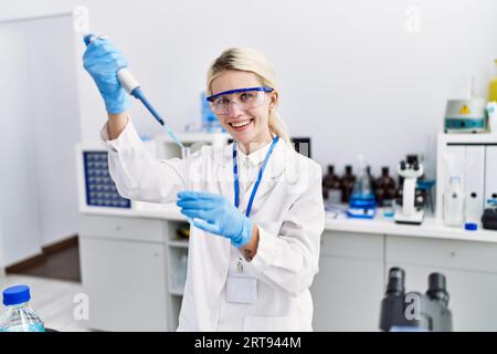 Junge blonde Wissenschaftlerin, die im Labor Flüssigkeit auf das Reagenzglas gießt Stockfoto