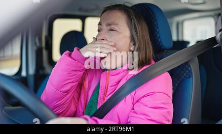 Reife hispanische Frau mit grauen Haaren, die ein Auto fährt und auf der Straße gähnt Stockfoto