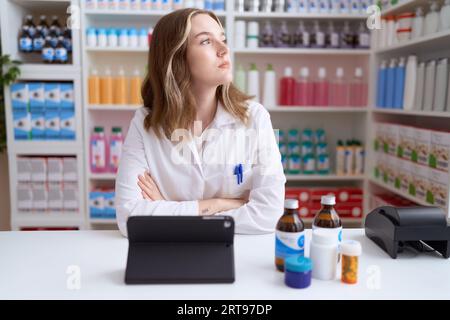 Junge kaukasische Frau, die in der Apotheke Drogerie arbeitet, indem sie Tablet zur Seite schaut, Profil entspannen, mit natürlichem Gesicht mit selbstbewusstem Lächeln posieren. Stockfoto