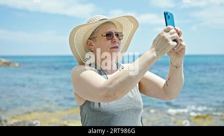 Mittelalter grauhaarige Frau Touristen machen Foto mit dem Smartphone am Strand Stockfoto