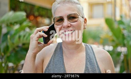 Grauhaarige Frau mittleren Alters lächelt selbstbewusst auf dem Smartphone im Park Stockfoto