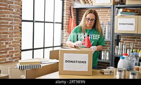 Mittelalte hispanische Frau, die freiwillig Pappkarton verpackt, um im Wohltätigkeitszentrum zu spenden Stockfoto