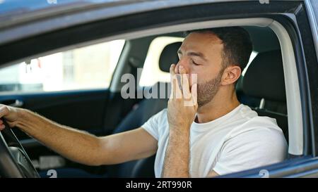 Ein junger latino, der ein Auto fährt, gähnt auf der Straße Stockfoto