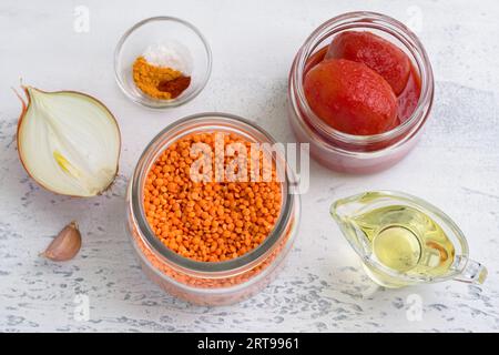 Zutaten für vegane Tomatenlinsensauce, Suppe oder für Linsenpfannkuchen: Rote Linsen, Zwiebeln, Knoblauch, Tomaten in Dosen, Gewürze und Pflanzenöl auf einem li Stockfoto