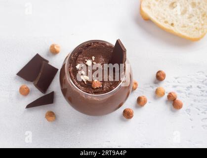 Vegane Schokoladenpaste mit Bananen und Nüssen, umgeben von Zutaten: Schokolade und Haselnüsse auf hellgrauem Hintergrund, Draufsicht Stockfoto