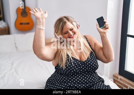 Junge Frau sitzt auf dem Bett, hört Musik und tanzt im Schlafzimmer Stockfoto