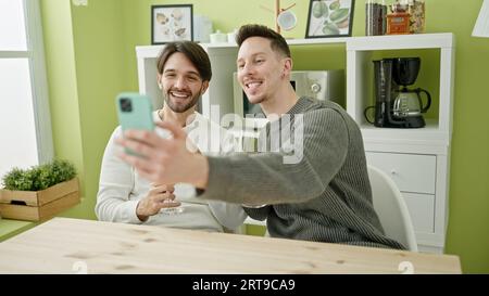 Zwei Männer, die ein Selfie-Foto mit dem Smartphone machen und ein Glas Wein im Speisesaal trinken Stockfoto