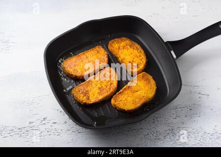 Süße gebratene Kürbistoasts mit Ingwer und Zimt in einer Pfanne auf einem hellblauen Tisch, Blick von oben. Kochbühne. Stockfoto