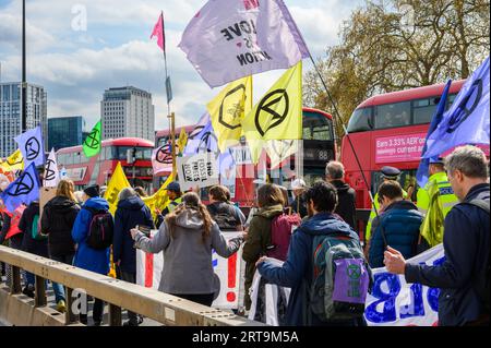 LONDON - 24. April 2023: Erleben Sie einen farbenfrohen protestmarsch der Extinction Rebellion auf der Waterloo Bridge mit den berühmten Londoner Doppeldeckerbussen in der BA Stockfoto