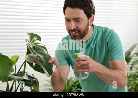 Mann, der schöne Topfpflanzen mit Wasser drinnen besprüht Stockfoto