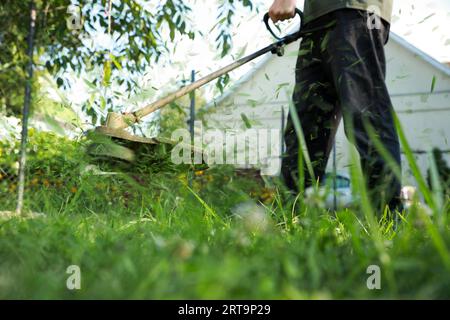 Ein Mann, der grünes Gras mit einem Rasentrimmer im Freien mäht, Nahaufnahme Stockfoto