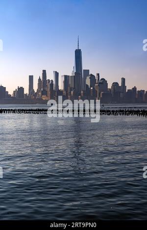 New York, NY - US - 7. September 2023 Vertikaler Sonnenaufgangsblick auf Lower Manhattan über den Hudson River mit Reflexionen der Skyline. Reste eines Pier Stockfoto