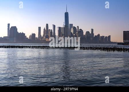 New York, NY - US - 7. September 2023 Sonnenaufgang mit Blick auf Lower Manhattan über den Hudson River mit Reflexionen der Skyline. Reste eines Pier Stockfoto