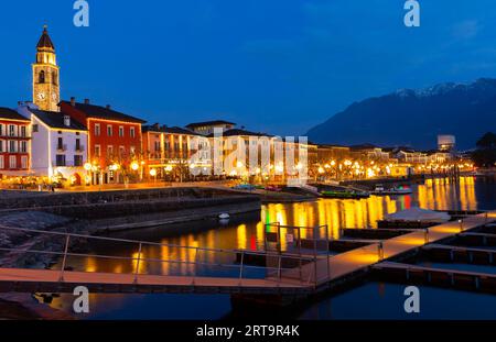 Beleuchtete Promenade in Ascona mit Glockenturm und festfahrenden Booten in der Dämmerung Stockfoto