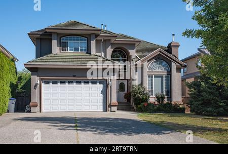 Außenfassade des Hauses an einem sonnigen Tag. Großes, maßgeschneidertes Luxushaus mit schön angelegtem Vorgarten und Einfahrt zur Garage in Vororten. Mod Stockfoto