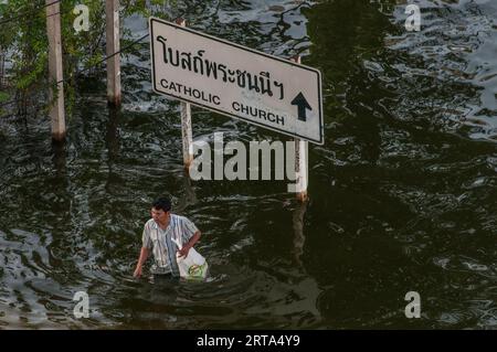 Der thailändische Mann weht die überflutete Straße entlang, vorbei an einem zweisprachigen Richtungsschild in Rangsit, einem nördlichen Vorort von Bangkok, Thailand. November 2011. © Kraig Lieb Stockfoto