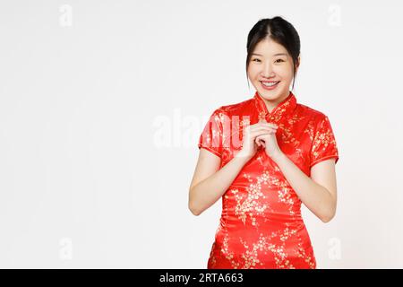Glückliches chinesisches Neujahr. Asiatische Frau trägt traditionelles Cheongsam Qipao Kleid mit Glückwunschgeste isoliert auf weißem Hintergrund. Stockfoto