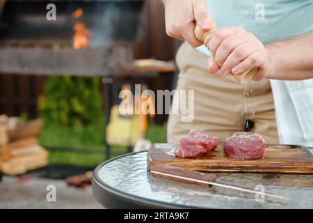 Nicht erkennbarer Mann, der mit der Handmühle rohes Streifensteak mit Salz würzt (Foto mit geringer Feldtiefe) Stockfoto