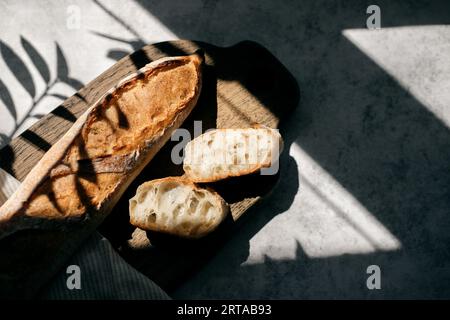 Blick von oben auf französisches Baguette mit frischen Broten und Scheiben auf einer Keramikplatte auf grauem Hintergrund in der Küche. Stockfoto