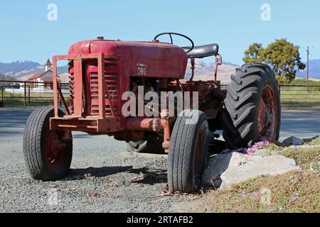 Antiker und alter rostroter Traktor in Kalifornien USA, typisches Landwirtschaftsfahrzeug mit einem Curch-Gebäude im Hintergrund Stockfoto