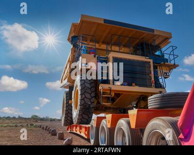 Industrietransporter mit einem riesigen Bergbaufahrzeug auf einer unbefestigten Straße im Outback, sonniger Tag Stockfoto