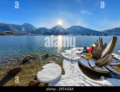 Wanderfrau sitzend auf Holzlotusblumen am Wolfgangsee mit Strobl und Rettenkogel im Hintergrund, Wolfgangsee, Salzkammergut, Salzkammerg Stockfoto